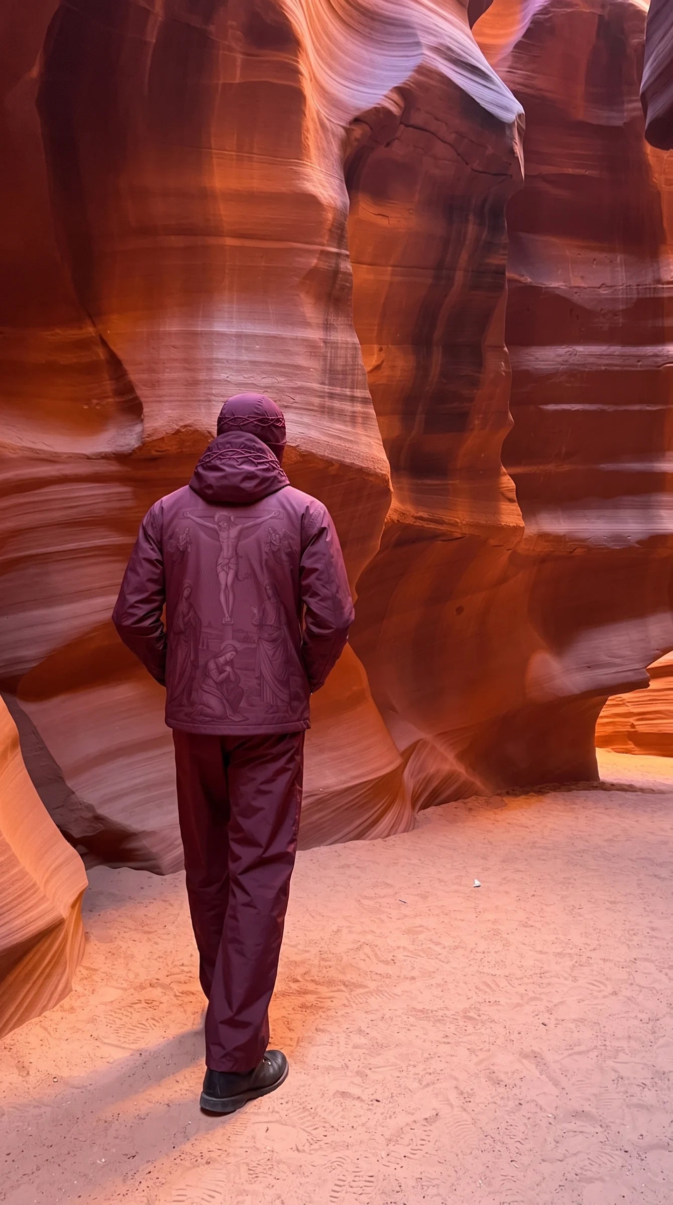 The burgundy LUKAS Rain Shell, seen from behind, inside a red sandstone canyon.